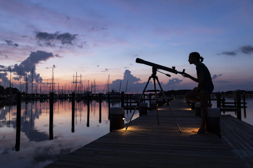 young person watching the sky at dusk with telescope